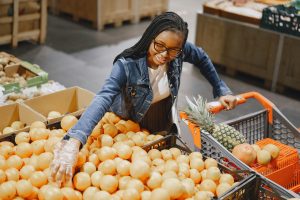 Smiling woman selecting fresh citrus fruits in a grocery store, enjoying a vibrant shopping experience.
